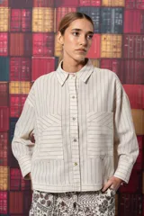 Camisa beige con rayas verticales negras, cuello clásico, cierre frontal con botones y dos bolsillos con solapa en el pecho.