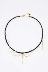 Collar de cuentas de cristal facetado negro con detalles de cadenas doradas colgantes.