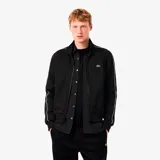Campera deportiva Lacoste de corte regular, color negro con cierre frontal completo y cuello alto. Presenta detalles de líneas blancas en los hombros y mangas, puños y ruedo acanalados, y el logo del cocodrilo bordado en el pecho.