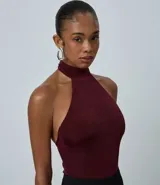 Body de mujer con diseño halter, confeccionado en tejido rib acanalado con acabado brillante. Presenta cuello alto con cierre posterior, corte ajustado al cuerpo y diseño sin mangas.