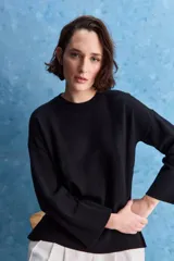 Sweater de tejido negro con cuello redondo, mangas amplias acampanadas y detalles de textura horizontal. Presenta una silueta holgada y relajada.
