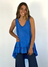 Top sin mangas de color azul confeccionado en algodón, con escote en V, silueta amplia y detalle de volado en el ruedo asimétrico.