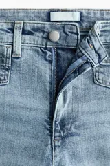 Jean tobillero de denim de algodón con leve stretch, piernas amplias, tiro alto, bolsillos parche delanteros con botón y corte holgado de muslo a bajo.