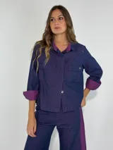 Chaqueta azul con cuello y puños color lila, de corte recto, con mangas 3/4, cierre frontal con botones y bolsillos delanteros con solapa.