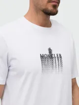 Remera de algodón blanca con cuello redondo y manga corta. Presenta un estampado frontal con el logo de la marca en efecto distorsionado y un parche circular con el logo en la manga.