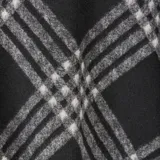 Poncho abierto con diseño de cuadros escoceses en tonos negro, gris y blanco. Presenta bordes con flecos largos y una caída fluida sobre los hombros.