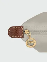 Mochila de diseño minimalista en color beige, con solapa y asa superior en cuero marrón texturizado. Cuenta con correas ajustables en color marrón y cierre principal.