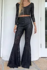 Top corto confeccionado en cuero negro con mangas largas de encaje floral. Presenta escote en V, diseño entallado con costuras decorativas y cierre frontal mediante botones metálicos.