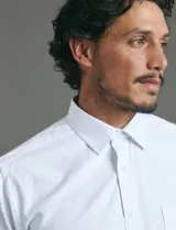 Camisa de vestir blanca de manga larga, con cuello clásico, cierre frontal de botones y bolsillo en el pecho.