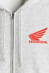 Campera con capucha gris melange de felpa con interior cepillado, cierre frontal, hombros caídos y bolsillos tipo canguro. Presenta estampado pequeño de Honda en el pecho.