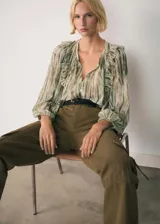 Blusa de tejido fluido con estampado abstracto en tonos verdes y beige, cuello redondo con volados, mangas largas con puños elásticos y cierre frontal con botones.