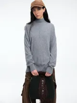 Sweater de tejido de punto color marrón, con cuello alto, corte amplio y tajos laterales en el ruedo. Presenta una costura vertical central en el frente y mangas largas con puños acanalados.