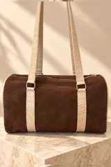 Cartera tipo baulito de cuero color marrón tostado, con doble asa larga de hombro, cierre superior y detalle de placa metálica con el logo de la marca en el centro.