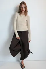 Pantalón culotte de tiro medio, color verde militar, con cintura elástica y bolsillos laterales ocultos. Presenta un diseño de bajo ancho con aberturas ajustables mediante cordones fruncidos en los laterales.