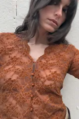 Top de manga larga color marrón óxido, confeccionado en tejido de encaje floral. Presenta escote en V con cierre frontal de botones pequeños.