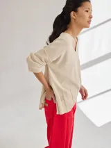 Buzo de tejido de punto liviano en color beige, con escote en V y diseño holgado. Presenta costuras visibles en los hombros y un detalle bordado en el lateral inferior.