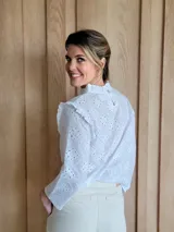 Blusa blanca de manga larga con cuello alto y volados en cuello y hombros.