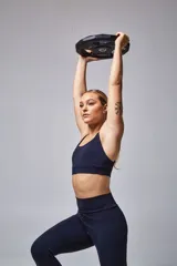 Top deportivo color beige con contorno inferior y tiras cruzadas en la espalda color borgoña. Cuenta con almohadillas removibles.