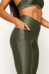 Calza deportiva de tiro alto en color verde militar, confeccionada en tejido técnico con acabado satinado. Presenta un diseño anatómico que se ajusta al cuerpo y cuenta con un bolsillo interno.