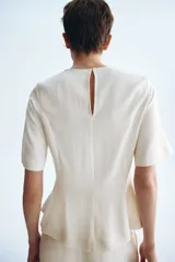 Blusa blanca de manga corta con escote redondo, costuras moldeadoras y diseño peplum acampanado con cierre trasero de botón.