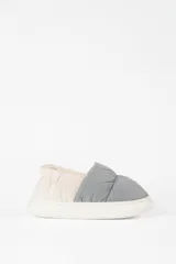 Pantufla tipo slip-on con diseño acolchado, combinando paneles en color gris y beige. Cuenta con interior forrado en material suave y suela de goma blanca.