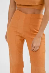 Pantalón de tiro alto con corte flare, confeccionado en lino color naranja. Presenta costuras verticales frontales que estilizan la silueta.