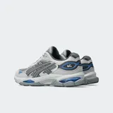 Championes Asics modelo Gel NYC 2.0, con diseño inspirado en el running de alto rendimiento. Presenta una combinación de malla y superposiciones de gamuza en tonos grises, con detalles en azul vibrante. Incorpora tecnología GEL y amortiguación FF BLAST PLUS en la mediasuela para mayor confort.