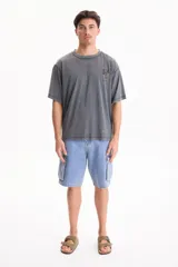 Remera oversize gris de manga corta con efecto lavado acid wash y estampa pequeña en el pecho con la palabra 'START' dentro de un recuadro amarillo.