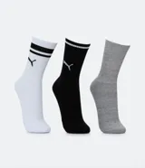 Kit de tres pares de medias deportivas Puma de caña larga. Un par es beige con dos rayas marrones y logo de Puma. Otro par es blanco liso. El tercer par es marrón oscuro con dos rayas blancas y logo de Puma. Todas están confeccionadas en algodón.