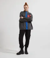 Campera larga de poliéster color gris con cierre frontal en tono azul vibrante, cuello alto, bolsillo en el pecho con solapa fucsia y detalles en naranja. Diseño holgado.