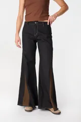 Pantalón de jean de pierna ancha con cortes laterales y paneles triangulares en contraste de color marrón. Presenta costuras a la vista en tono ocre y ruedo desflecado.