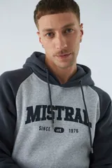 Buzo canguro gris con mangas ranglan azul marino, capucha con cordones ajustables y bolsillo delantero. Estampado frontal con el logo de la marca y el año de fundación.