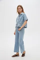 Blusa de jean de manga corta, corte holgado, con cuello en V, cierre frontal con botones y detalles de frunces.