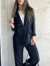 Blazer negro con finas rayas verticales blancas, solapas de muesca, cierre frontal con un botón y bolsillos laterales.