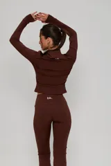 Conjunto deportivo de dos piezas color marrón, compuesto por una campera de cuello alto con cierre frontal y mangas largas con abertura para pulgar, y un pantalón de corte ajustado con terminación acampanada.