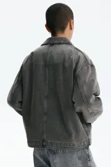 Campera de denim de algodón rígido, color gris oscuro con efecto gastado, cuello clásico, hombros caídos y cierre frontal. Cuenta con bolsillos delanteros ribeteados, un bolsillo superior con cierre y bajo recto.