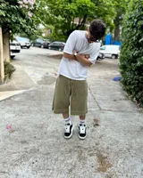 Bermuda de corte baggy color verde con efecto gastado. Presenta costura vertical trasera en cada pierna y detalle artesanal visible en el bajo. Incluye un cordón extra confeccionado en la misma tela.