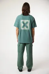 Remera de manga corta color gris, con cuello redondo y un pequeño parche cuadrado con una cruz estampada en el pecho.