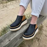 Zapatos de cuero color negro con paneles laterales en marrón y talón en marfil, con suela track alta y gruesa en tonos blanco y tostado.
