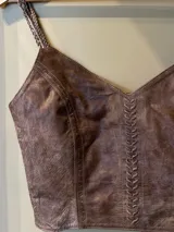 Top de cuero color marrón con escote en V y tirantes finos trenzados. Cuenta con un detalle vertical de pasamanería artesanal bordada a mano en el frente y cierre con broches en la espalda.