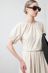 Top negro con escote redondo al frente y mangas cortas abullonadas con elástico en el puño. Presenta un detalle de abertura y lazo en la espalda.