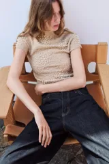 Top de punto color beige con cuello subido, manga corta y diseño texturizado con efecto arrugado. Presenta aplicaciones de perlas distribuidas en la parte frontal y las mangas.