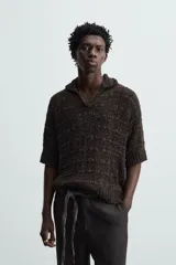 Polo de punto de calce relajado, color marrón oscuro jaspeado con negro. Presenta cuello solapa con abertura frontal en V y mangas cortas.