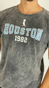 Remera de algodón con efecto lavado ácido en color gris, de corte clásico y manga corta. Presenta un estampado frontal con la palabra 'HOUSTON' en letras celestes con borde blanco, el número '1982' en blanco y un pequeño ícono superior.
