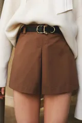 Short pollera mini de sarga color marrón, con pliegue frontal y cierre lateral oculto. Incluye un cinturón elástico a rayas con hebilla metálica redonda.