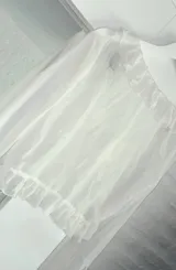Blusa blanca traslúcida con escote en V, volados en el contorno y mangas largas acampanadas con lazos en los puños.