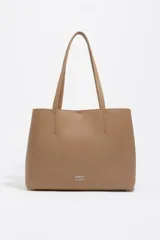 Bolso tote shopper de piel vacuna color camel, con textura granulada y asas de hombro. Presenta el logo metálico de Bimba y Lola en la parte inferior central.