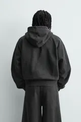 Sudadera con capucha y cierre frontal de cremallera, confeccionada en tejido de mezcla de algodón con interior afelpado. Presenta un diseño cropped, mangas largas, bolsillos frontales integrados en las costuras y acabados en rib. Posee un efecto lavado que le otorga una apariencia única.