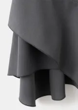 Vestido corto color gris oscuro, sin mangas y con cuello alto. Presenta un diseño entallado con panel fruncido en la cintura y falda asimétrica con volados.