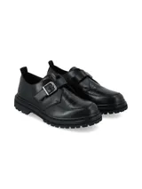 Zapato tipo monk strap de cuero negro con textura efecto cocodrilo en la puntera. Presenta una hebilla metálica ajustable en el empeine y una suela track dentada de goma.